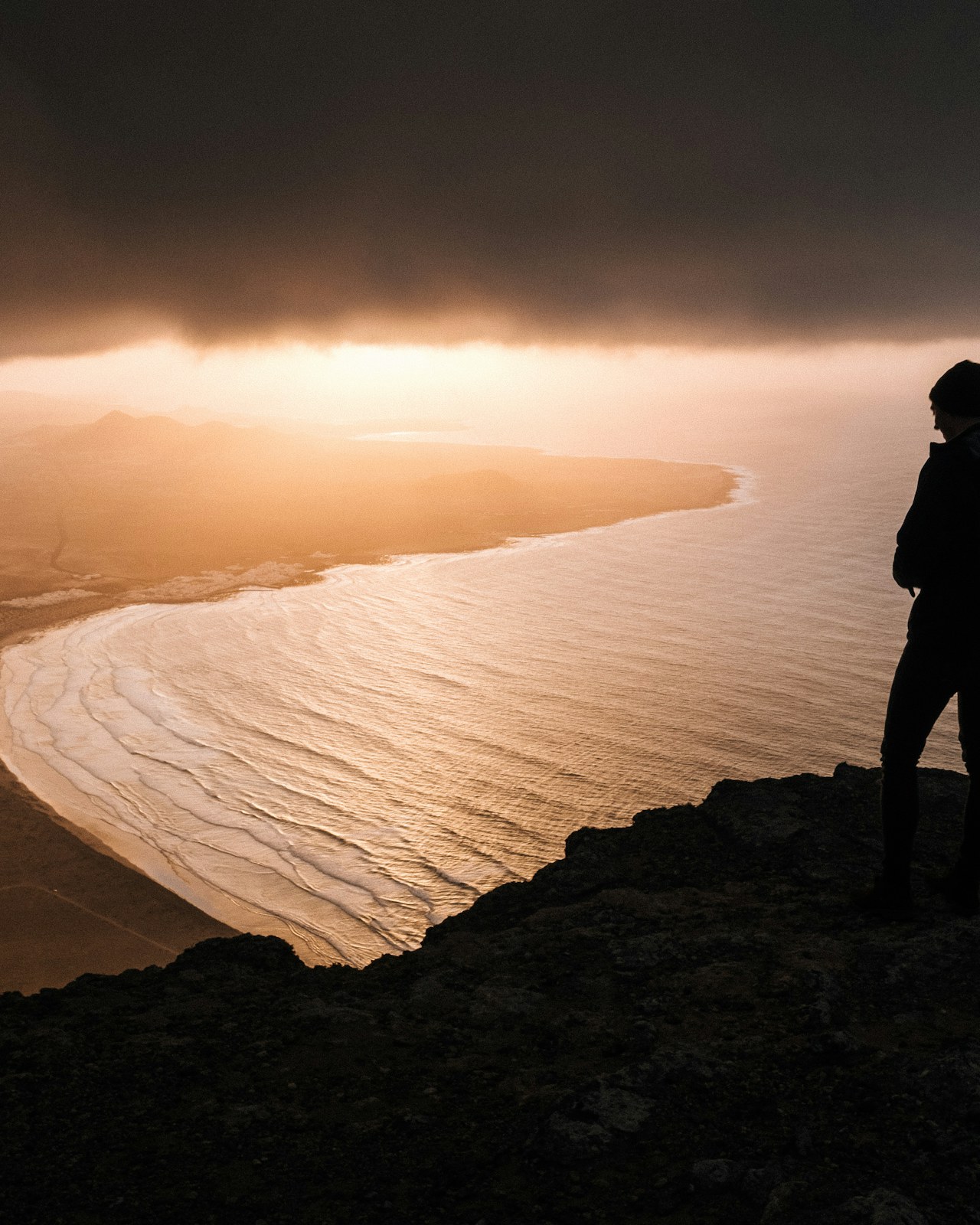 A person stands in silhouette looking toward a bright open horizon at dawn